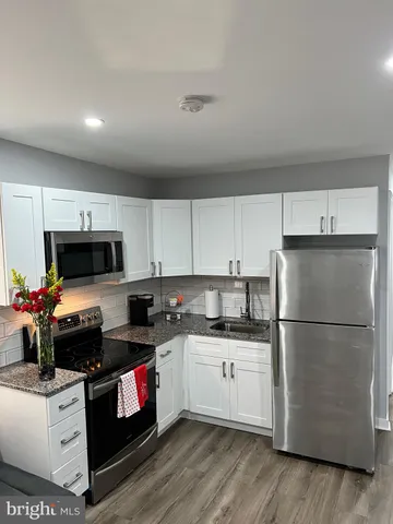 a kitchen with a refrigerator a stove top oven a sink dishwasher and white cabinets with wooden floor