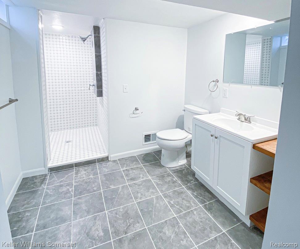 1821 Nazareth Road Kalamazoo, MI 49048 - Photo 16 of 20 Bathroom featuring a walk-in shower with patterned wall tile, gray floor tiling, a white vanity with integrated sink, and an exposed wood shelf unit