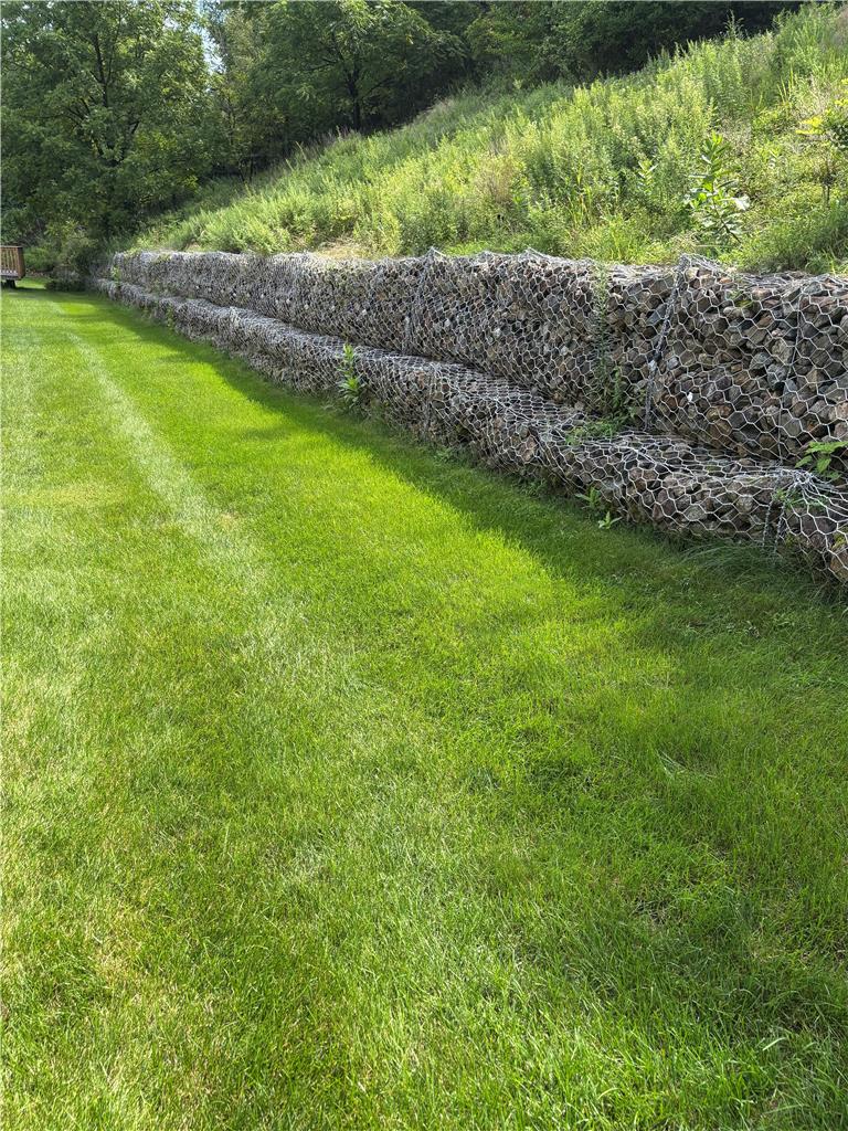 11 Abbey Road Easton, PA 18040 - Photo 7 of 24 A tiered gabion retaining wall borders a manicured green lawn beneath a grassy hillside.