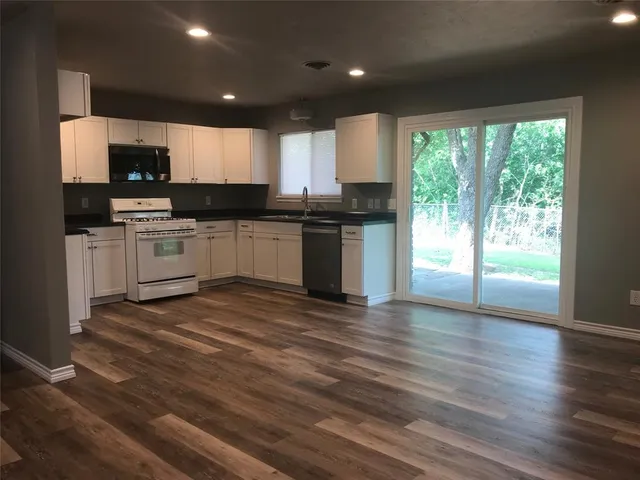 a large kitchen with kitchen island granite countertop a stove top oven a sink with wooden floors and wooden cabinets