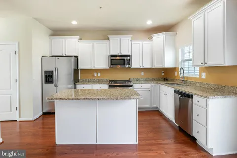 a kitchen with stainless steel appliances granite countertop a stove top oven a refrigerator a sink and white cabinets with wooden floor