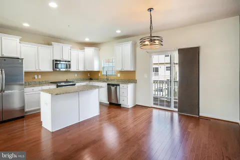 a kitchen with stainless steel appliances granite countertop a stove a sink a refrigerator and white cabinets with wooden floors