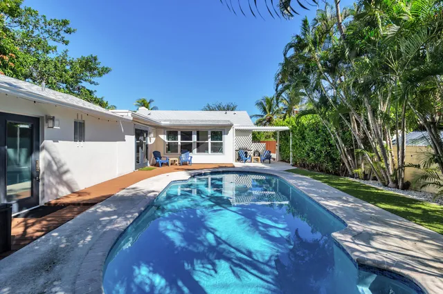 a view of a white house with swimming pool lawn chairs and a fire pit