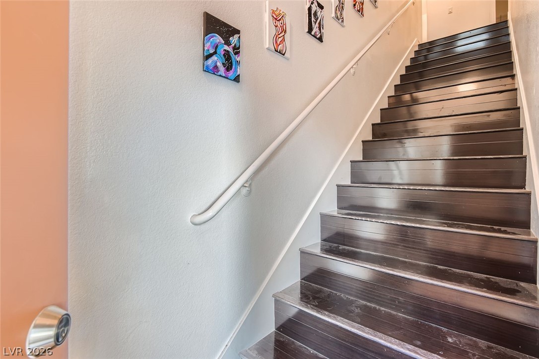 7701 West Robindale Road, Unit 265 Las Vegas, NV 89113 - Photo 4 of 27 Dark wood stairs lead upward beside a clean white wall with a mounted handrail.