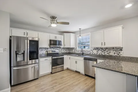 a kitchen with stainless steel appliances granite countertop a stove top oven a refrigerator a sink and dishwasher with wooden floor