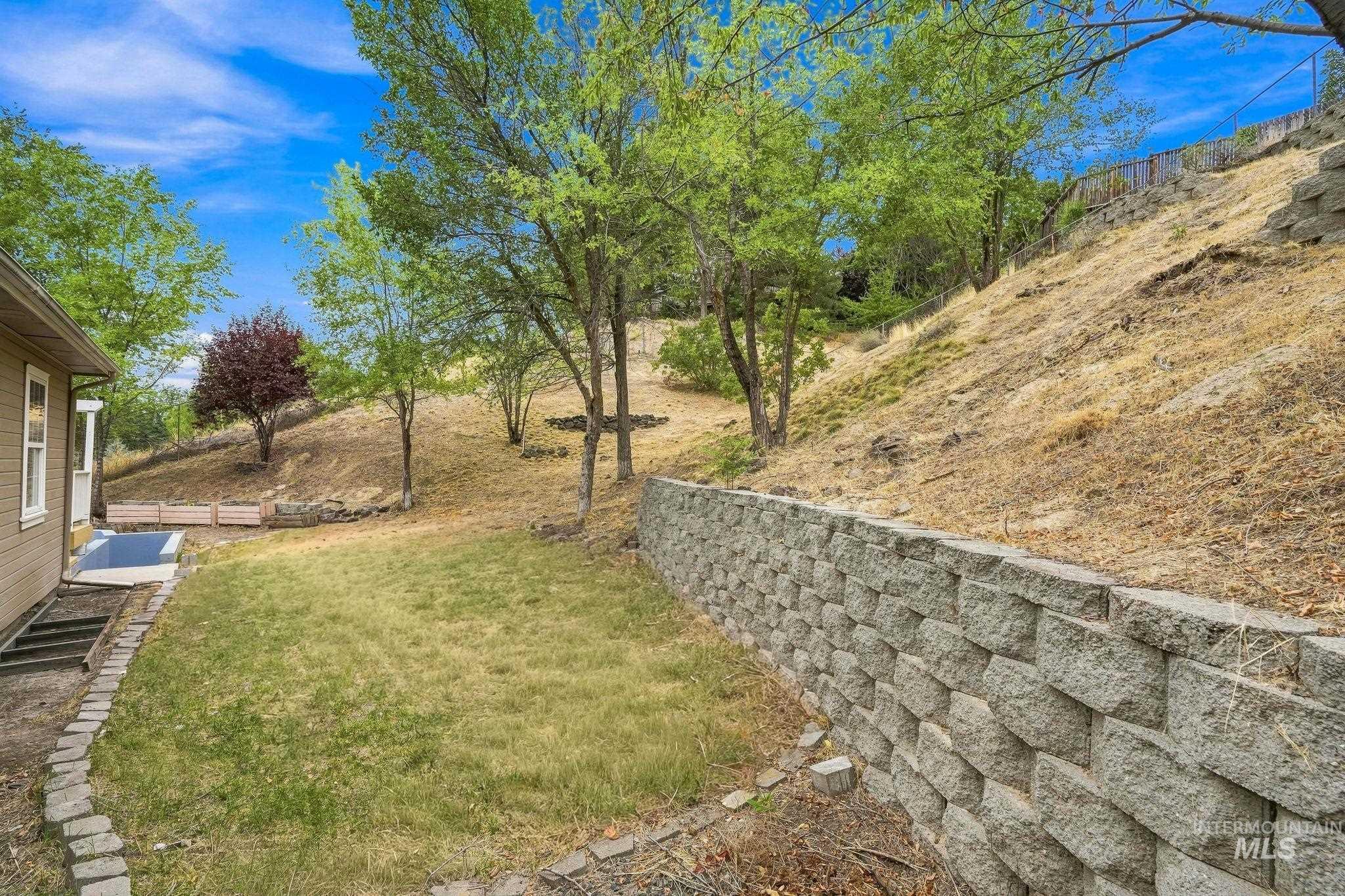 2442 West Hill Road Boise, ID 83702 - Photo 42 of 48 Sloped yard featuring a stone retaining wall, mature trees, and a grassy area