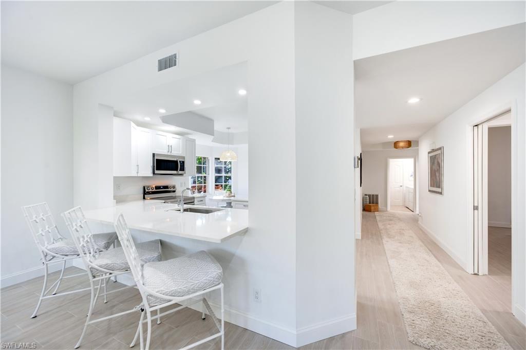2806 Aintree Lane, Unit H102 Naples, FL 34112 - Photo 7 of 26 Kitchen with light stone countertops, white cabinets, light wood-style flooring, a kitchen bar, and recessed lighting