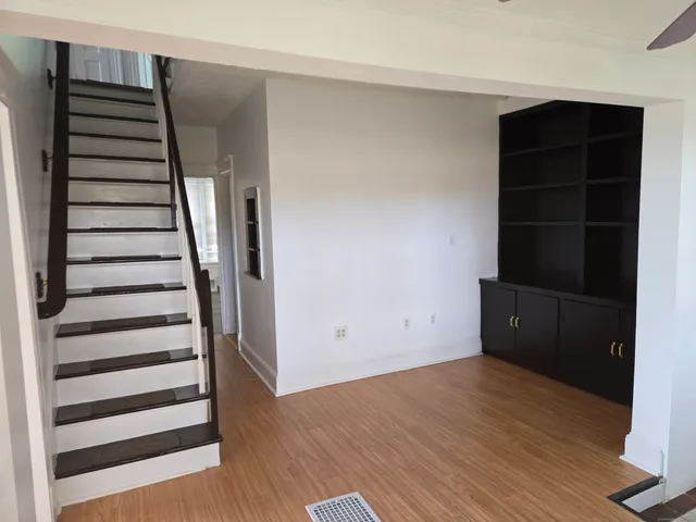 a view of an empty room with wooden floor and stairs
