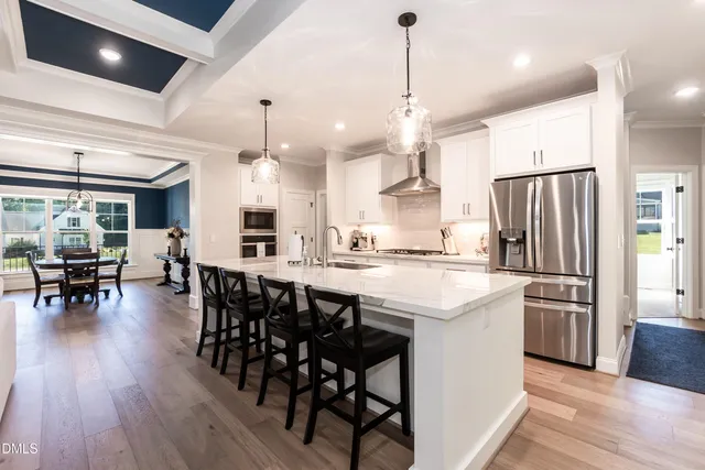 a kitchen with stainless steel appliances kitchen island granite countertop a dining table chairs stove and white cabinets