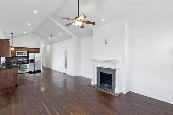 an empty room with wooden floor fireplace and kitchen view