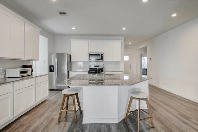 a kitchen with stainless steel appliances kitchen island granite countertop a refrigerator a stove a sink a dining table and chairs with wooden floor
