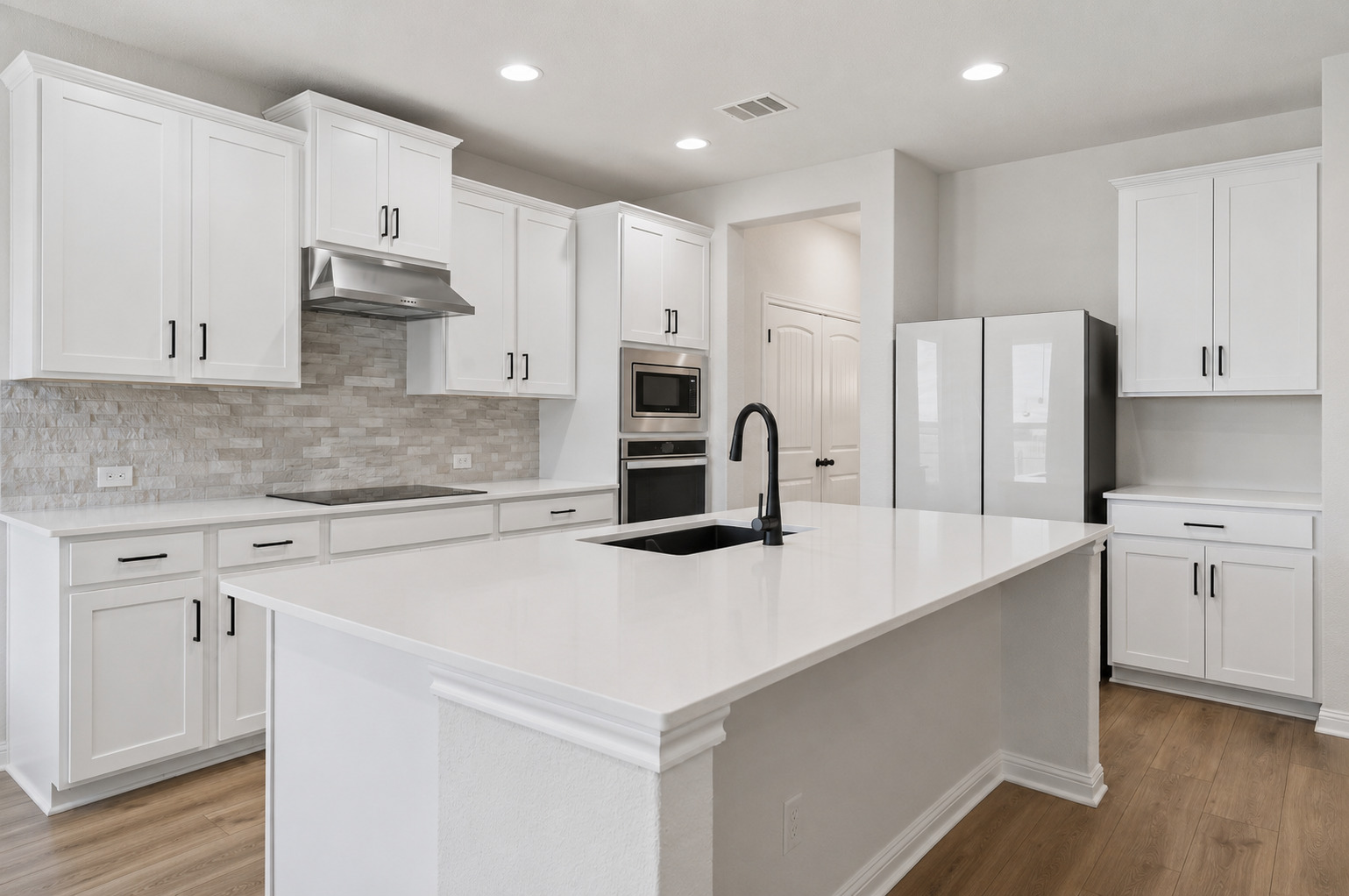 100 Panico Road Hutto, TX 78634 - Photo 5 of 28 White cabinetry and stone surfaces define this kitchen, centered around a large island with a sink.