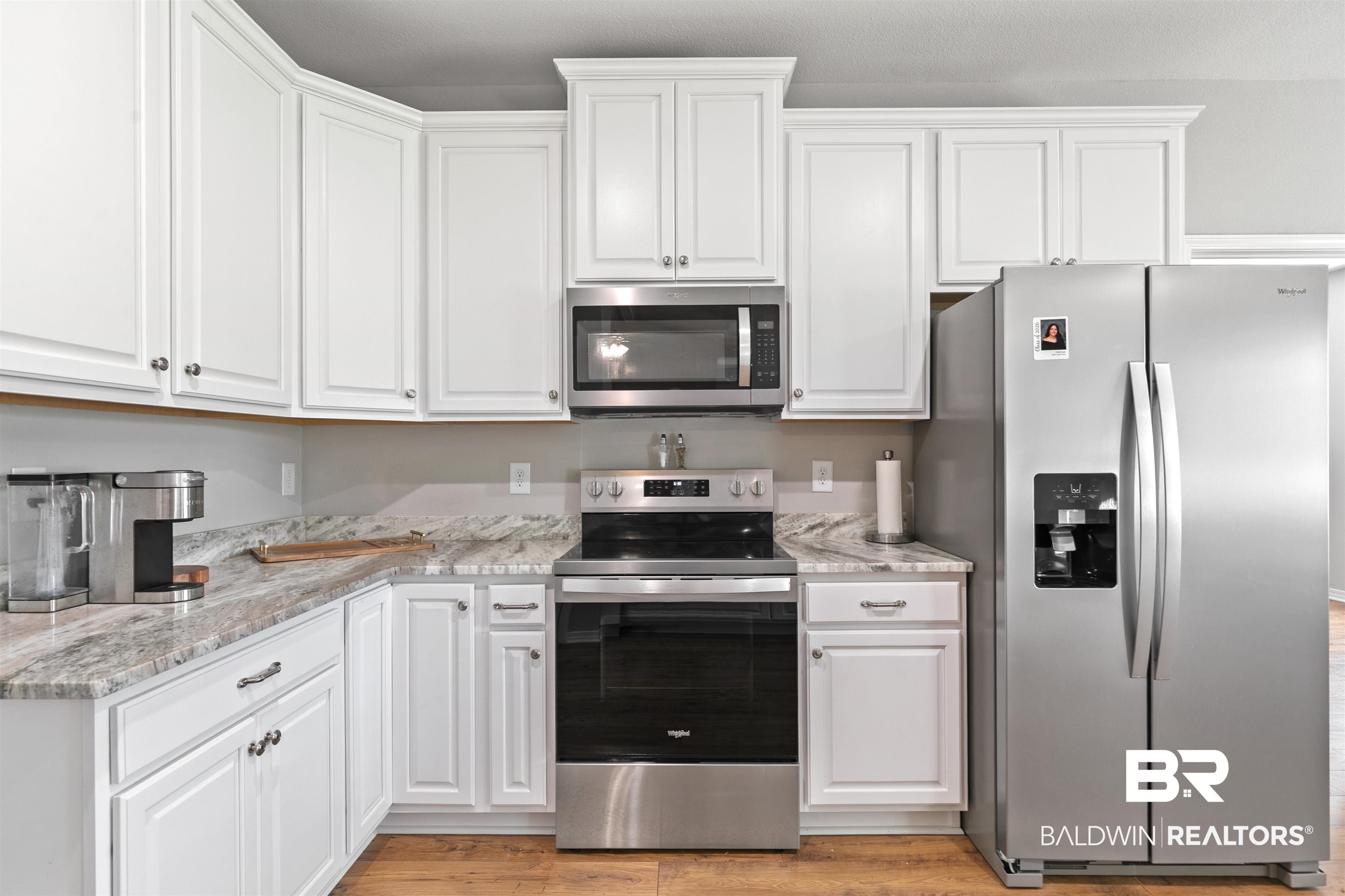 8552 March Road Irvington, AL 36544 - Photo 12 of 28 Kitchen featuring white shaker cabinetry, patterned countertops, stainless steel appliances, wood-finish flooring, and a microwave built-in above the range