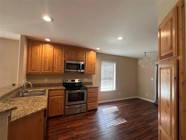 a kitchen with granite countertop wooden floors stainless steel appliances a window and a sink