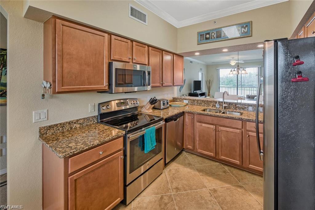 9731 Acqua Court, Unit 525 Naples, FL 34113 - Photo 8 of 35 Kitchen with stainless steel appliances, ornamental molding, brown cabinetry, dark stone countertops, and light tile patterned flooring