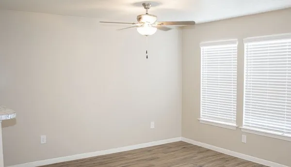 an empty room with wooden floor chandelier fan and windows