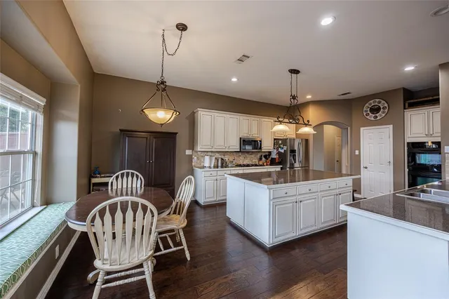 a kitchen with granite countertop kitchen island stainless steel appliances a dining table chairs sink and cabinets
