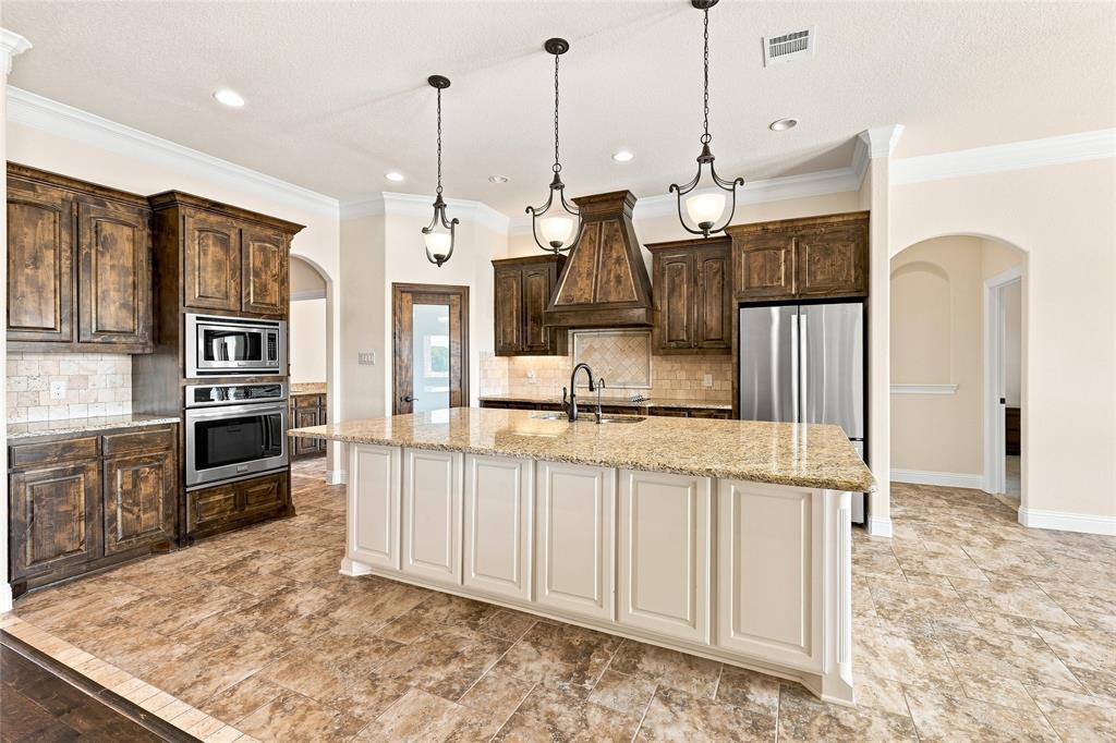 420 Hartley Way Azle, TX 76020 - Photo 12 of 40 Gourmet kitchen featuring a large central island with light-colored cabinetry, stainless steel appliances, dark wood-finish cabinetry, tile flooring, and decorative pendant lighting