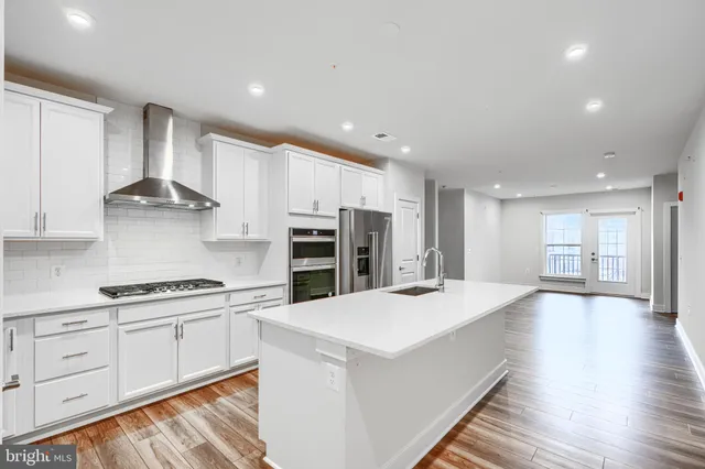 a kitchen with stainless steel appliances kitchen island granite countertop a stove a sink and white cabinets with wooden floor