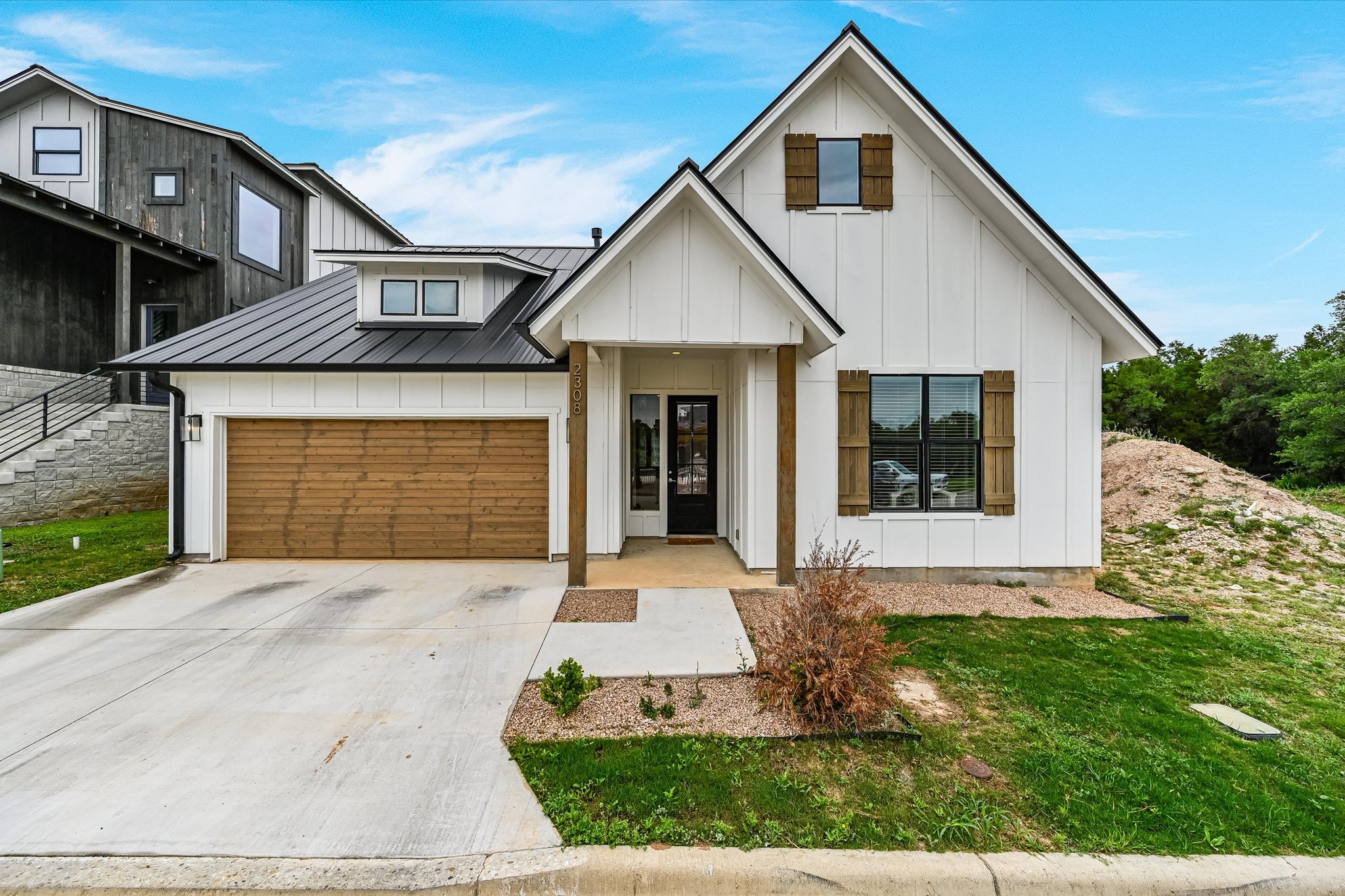 2308 Kellie Brooke Road, Unit 13 Spicewood, TX 78669 - Photo 1 of 19 The property features a white exterior with a black metal roof, a wood-paneled garage door, and a concrete driveway