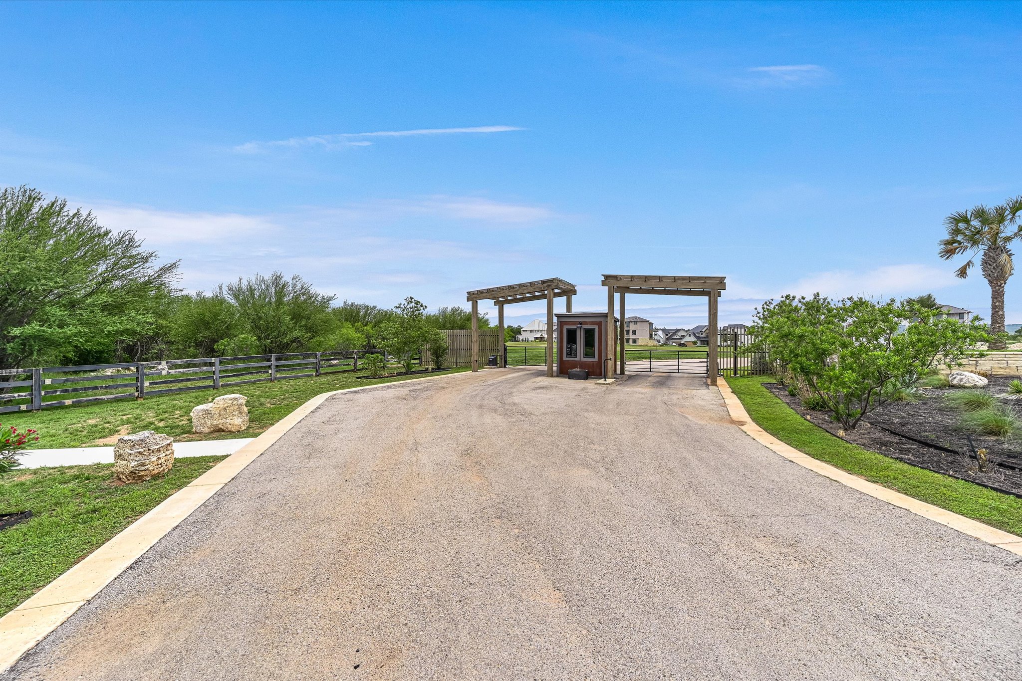 2308 Kellie Brooke Road, Unit 13 Spicewood, TX 78669 - Photo 19 of 19 The entrance features a paved driveway leading to a gate structure with wooden pergolas and a small building