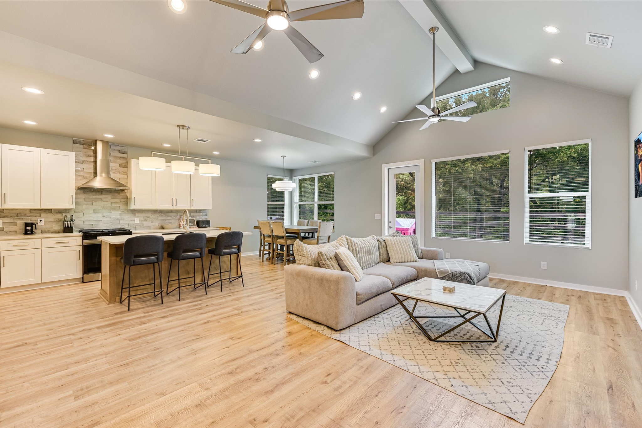 2308 Kellie Brooke Road, Unit 13 Spicewood, TX 78669 - Photo 2 of 19 This expansive open-concept living space features light wood-style flooring, a kitchen with white cabinetry and an island, and a living area with large windows providing natural light