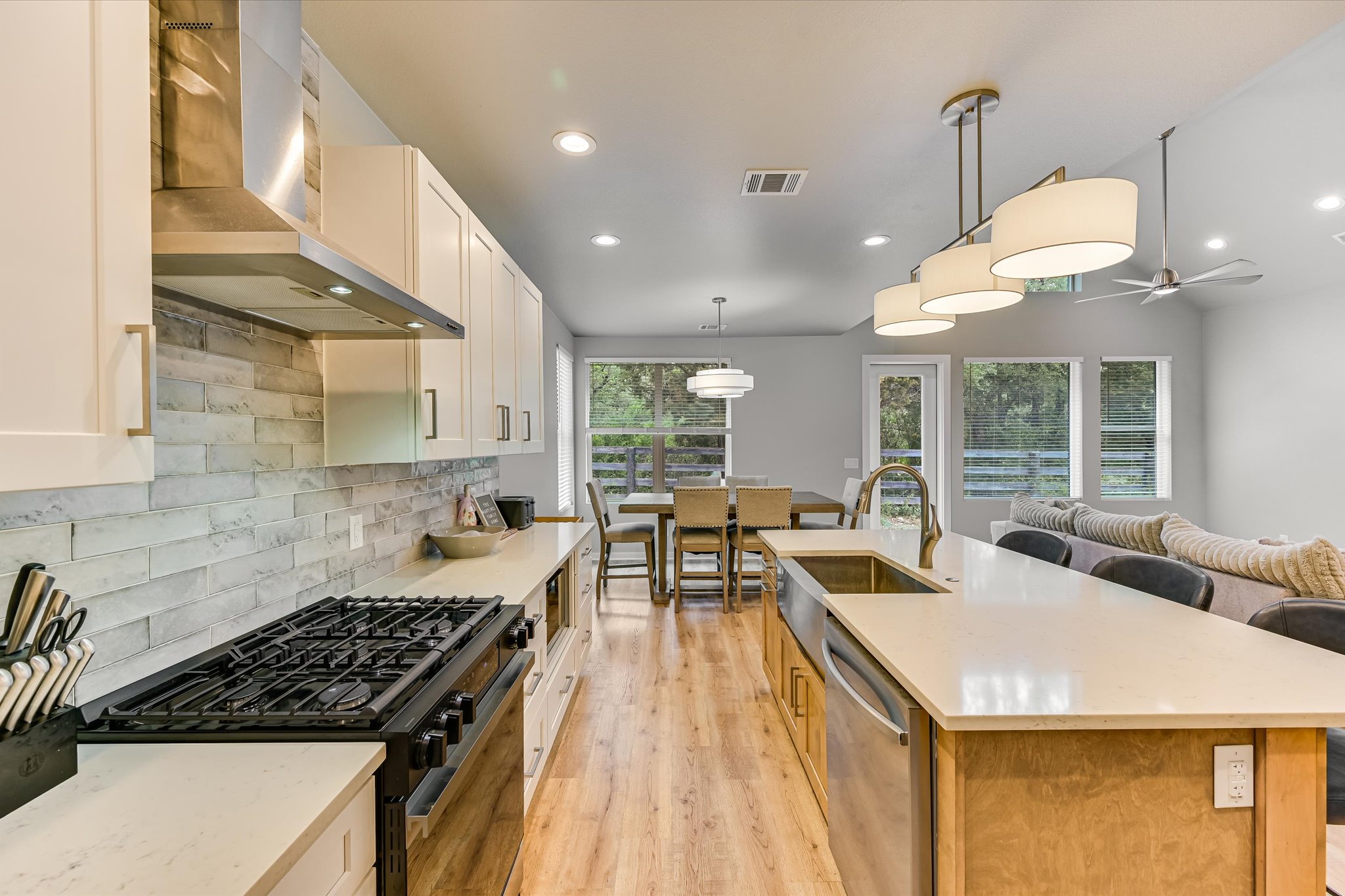 2308 Kellie Brooke Road, Unit 13 Spicewood, TX 78669 - Photo 7 of 19 The property features an open-concept kitchen with a gas range, white cabinetry, and a spacious island with a stainless steel sink