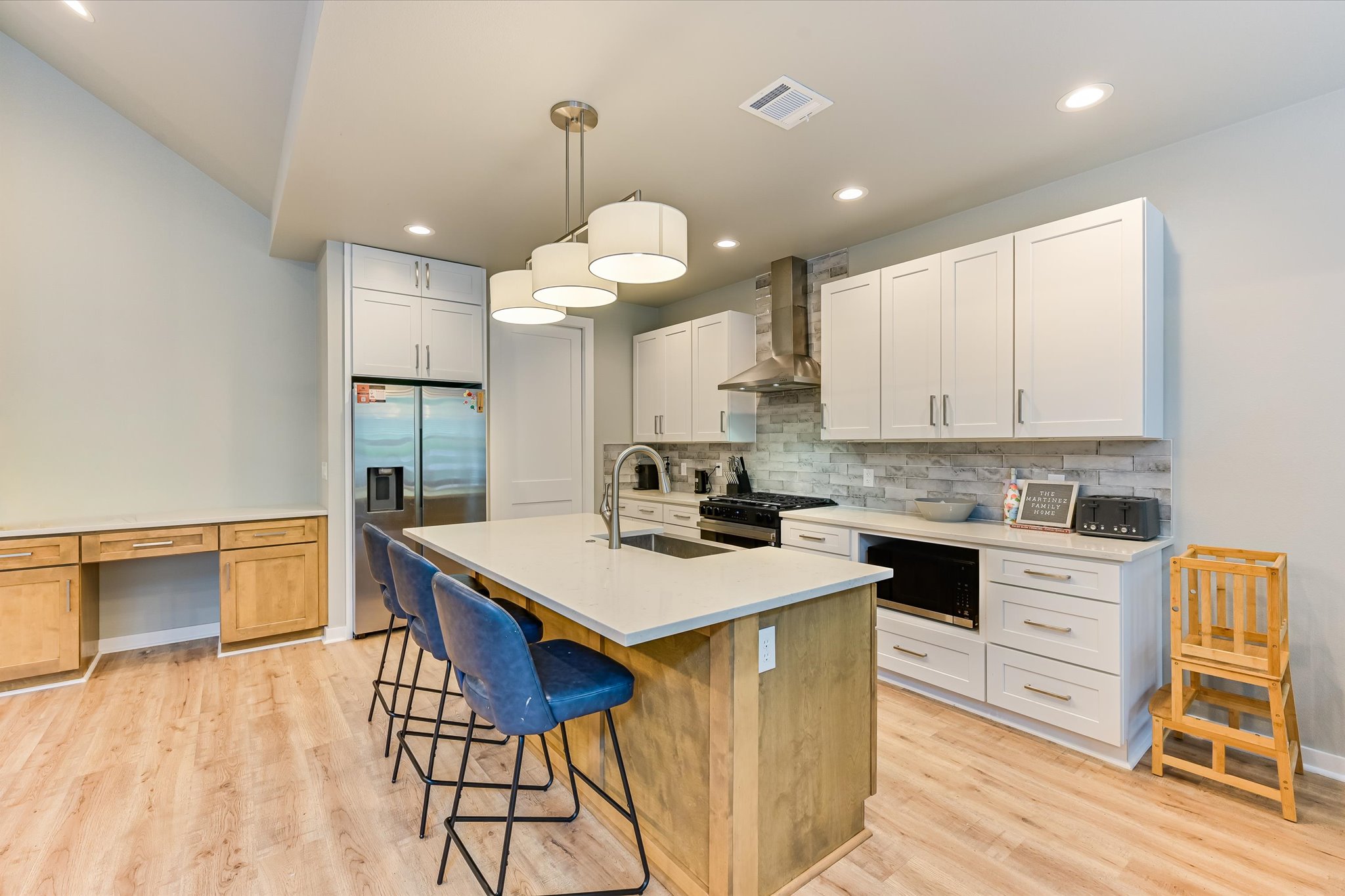 2308 Kellie Brooke Road, Unit 13 Spicewood, TX 78669 - Photo 8 of 19 The kitchen features a central island with a light-colored countertop and pendant lighting, white cabinetry, stainless steel appliances, and a light-toned wood-style floor