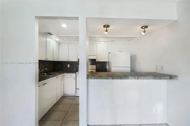 a large white kitchen with granite countertop a sink and dishwasher a stove with wooden floor