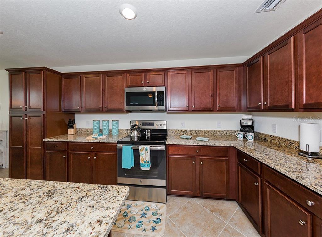 16904 Vardon Terrace, Unit 202 Lakewood Ranch, FL 34211 - Photo 22 of 30 a kitchen with kitchen island granite countertop a sink dishwasher stove top oven and wooden cabinets