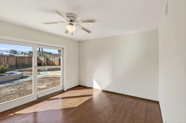 an empty room with wooden floor fan and windows