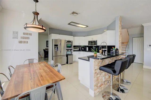 a kitchen with stainless steel appliances kitchen island granite countertop a table chairs and a refrigerator