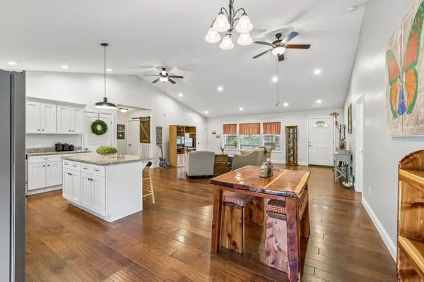 a kitchen with stainless steel appliances kitchen island granite countertop a stove a sink a refrigerator and white cabinets with wooden floor