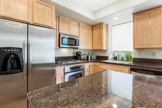 a kitchen with stainless steel appliances granite countertop a refrigerator a stove and a sink with wooden floor