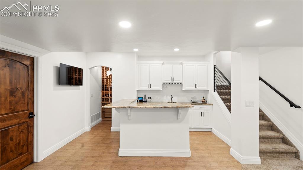 13625 Random Ridge View Colorado Springs, CO 80921 - Photo 26 of 50 Kitchen featuring light stone counters, white cabinets, recessed lighting, a breakfast bar area, and light wood-style flooring
