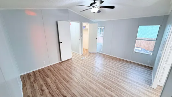 an empty room with wooden floor fan and windows