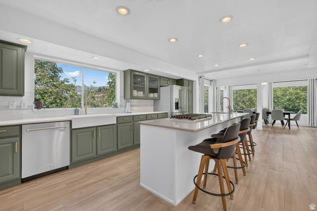 1979 Cave Hollow Way Bountiful, UT 84010 - Photo 13 of 59 Gourmet kitchen featuring sage-toned cabinetry, a large center island with counter seating, stainless steel appliances, a farmhouse sink, and wood-finish flooring