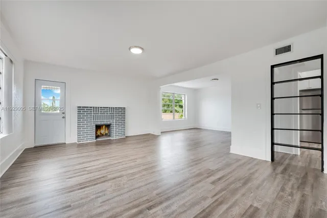 an empty room with wooden floor fireplace and windows