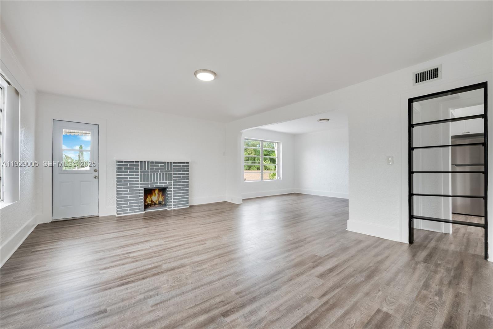 an empty room with wooden floor fireplace and windows