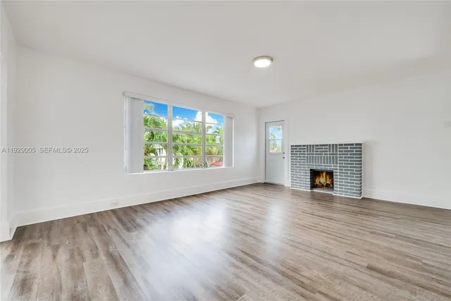 an empty room with wooden floor fireplace and windows