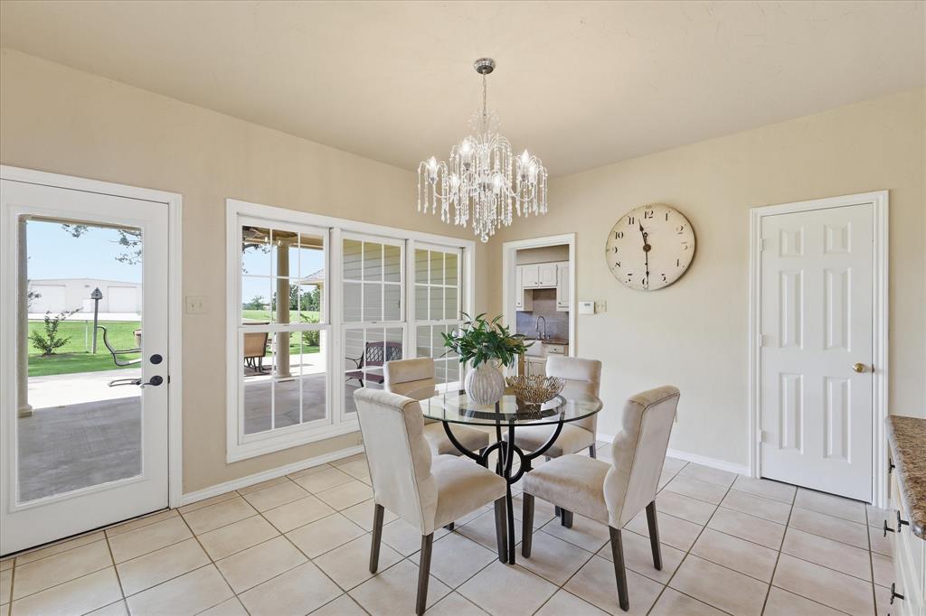 6955 Hawk Road Flower Mound, TX 75022 - Photo 19 of 40 Dining area featuring tile flooring, a crystal chandelier, multiple windows, a glass-top table, and a door leading to an outdoor patio