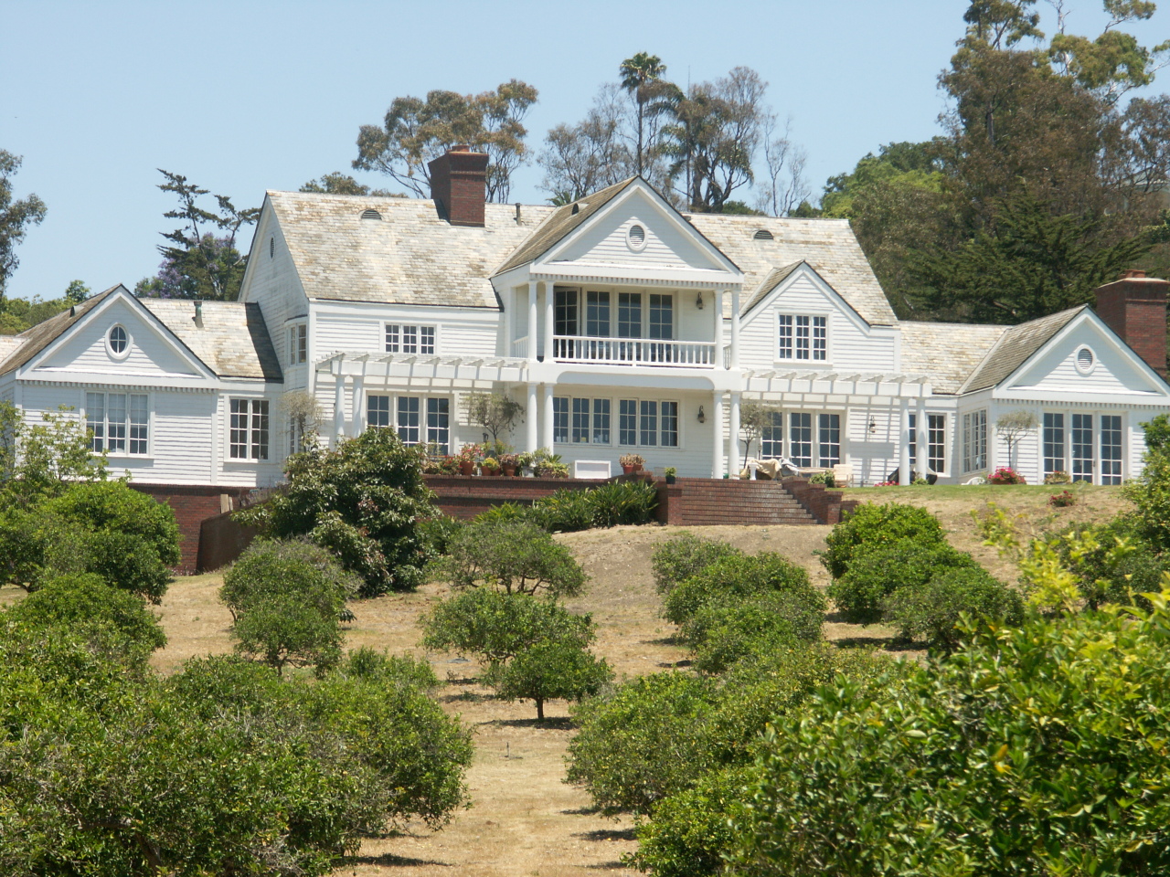 Undisclosed Address Hope Ranch, CA 93110 - Photo 8 of 17 a view of a white house next to a yard with plants and trees