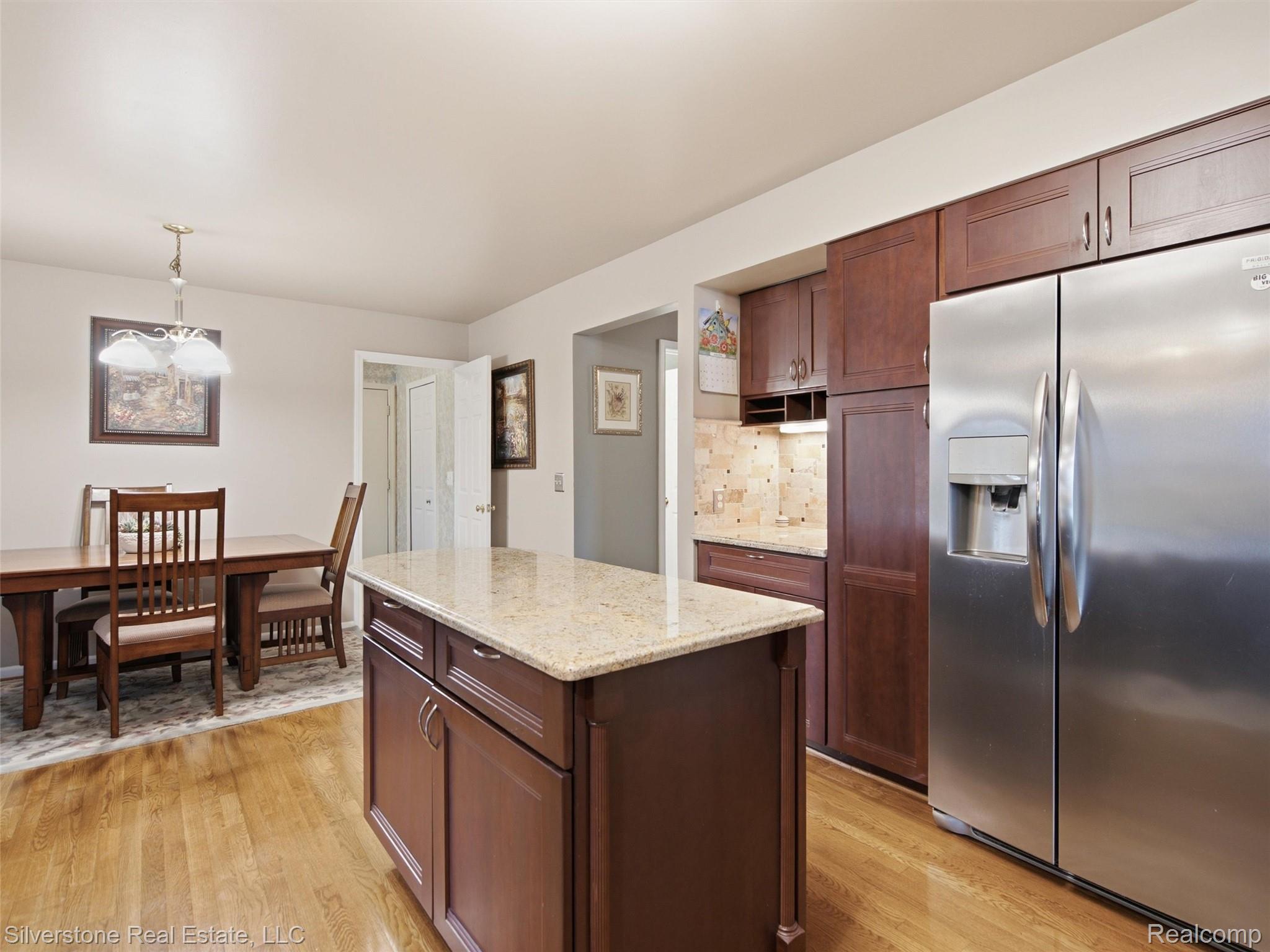 6577 Edith Court Troy, MI 48085 - Photo 23 of 61 Kitchen featuring wood-finish flooring, a central island with a light-toned countertop, dark wood cabinetry, a stainless steel refrigerator, and a tiled backsplash