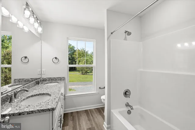 a bathroom with a granite countertop tub sink vanity mirror and a next to a window