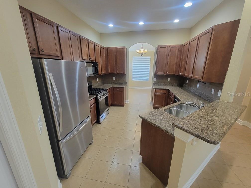 10418 Fenceline Road New Port Richey, FL 34655 - Photo 12 of 36 a kitchen with stainless steel appliances granite countertop a refrigerator a sink and wooden cabinets