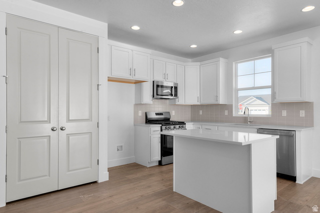 5644 Ibis Road Tooele, UT 84074 - Photo 15 of 19 Modern kitchen featuring white cabinetry, a central island with a solid surface countertop, stainless steel appliances, and wood-finish flooring