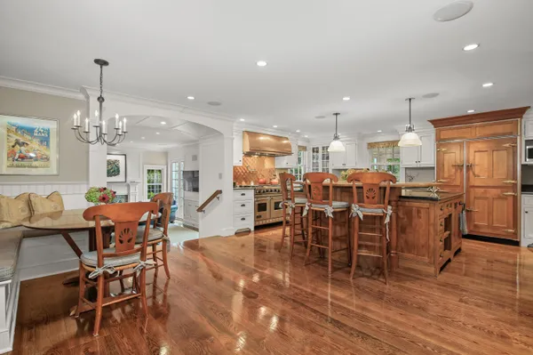 a kitchen with stainless steel appliances granite countertop a stove a refrigerator a kitchen island a dining table and chairs with wooden floor