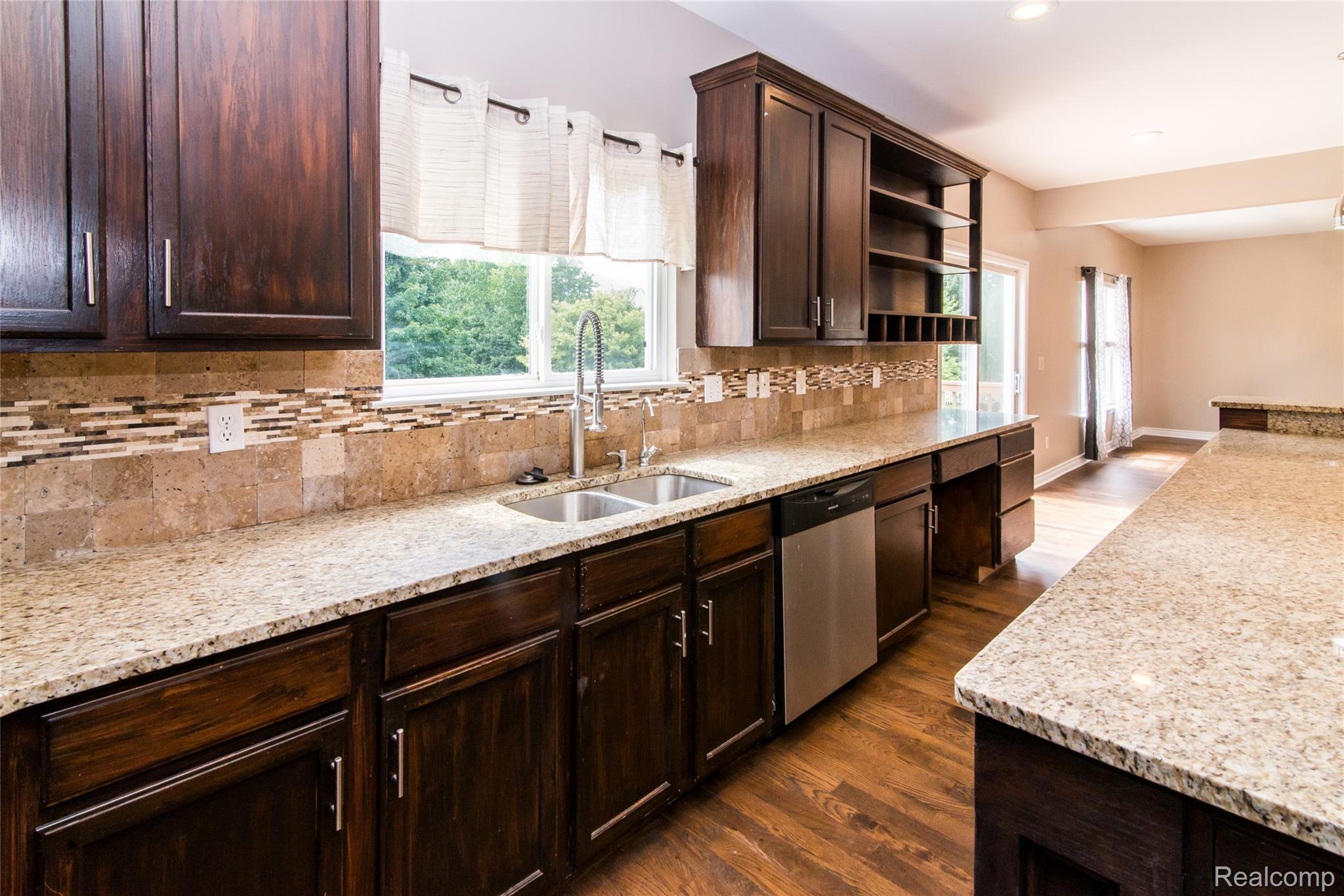 486 Sweet Briar Ridge Linden, MI 48451 - Photo 31 of 69 Spacious kitchen featuring dark wood cabinetry, light speckled countertops, a double basin sink with a high-arch faucet, a stainless steel dishwasher, and wood-finish flooring