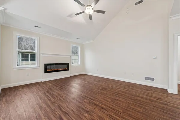an empty room with wooden floor chandelier fan and windows