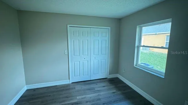 an empty room with wooden floor closet and windows